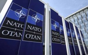 NATO toplantısında müttefik ülkelerin temsilcileri ve NATO bayrağı